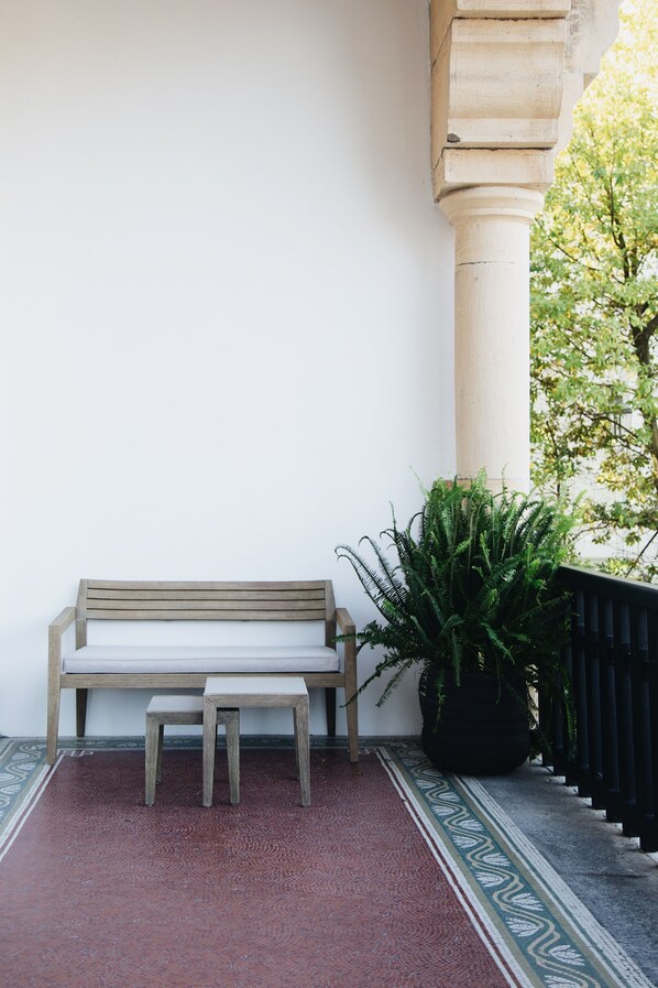 A bench and a small table in a covered outdoor area with a patterned floor, a large potted plant, and a column. - Bidaia Boutique Hotel (San Sebastián)