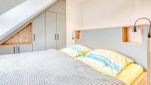 A bedroom with a sloped ceiling, built-in wardrobes, a bed with striped bedding, and bedside tables with lamps.