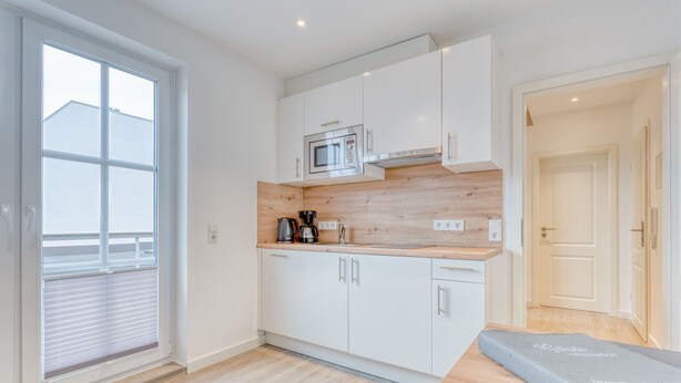 A modern kitchen with white cabinets, a built-in microwave, and a coffee maker.