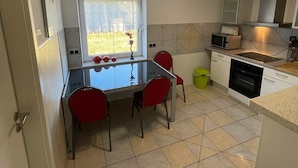 A compact kitchen with a dining table, chairs, a window, a microwave, a stove, and a trash bin. - ZV-Scholtz Gästehaus Neuötting (Neuoetting)