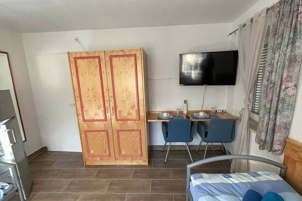 A hotel room with a bed, a desk with chairs, a TV, and a wardrobe.