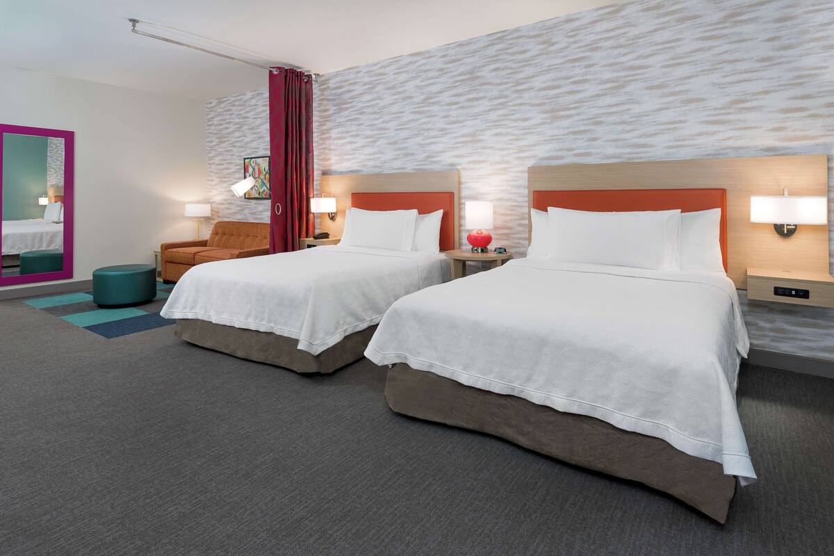 Habitación de hotel con dos camas, una silla, una mesita y una pared con textura.