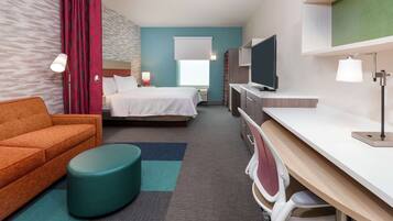 A hotel room with a bed, a sofa, a desk with a chair, a TV, and a window with a curtain.