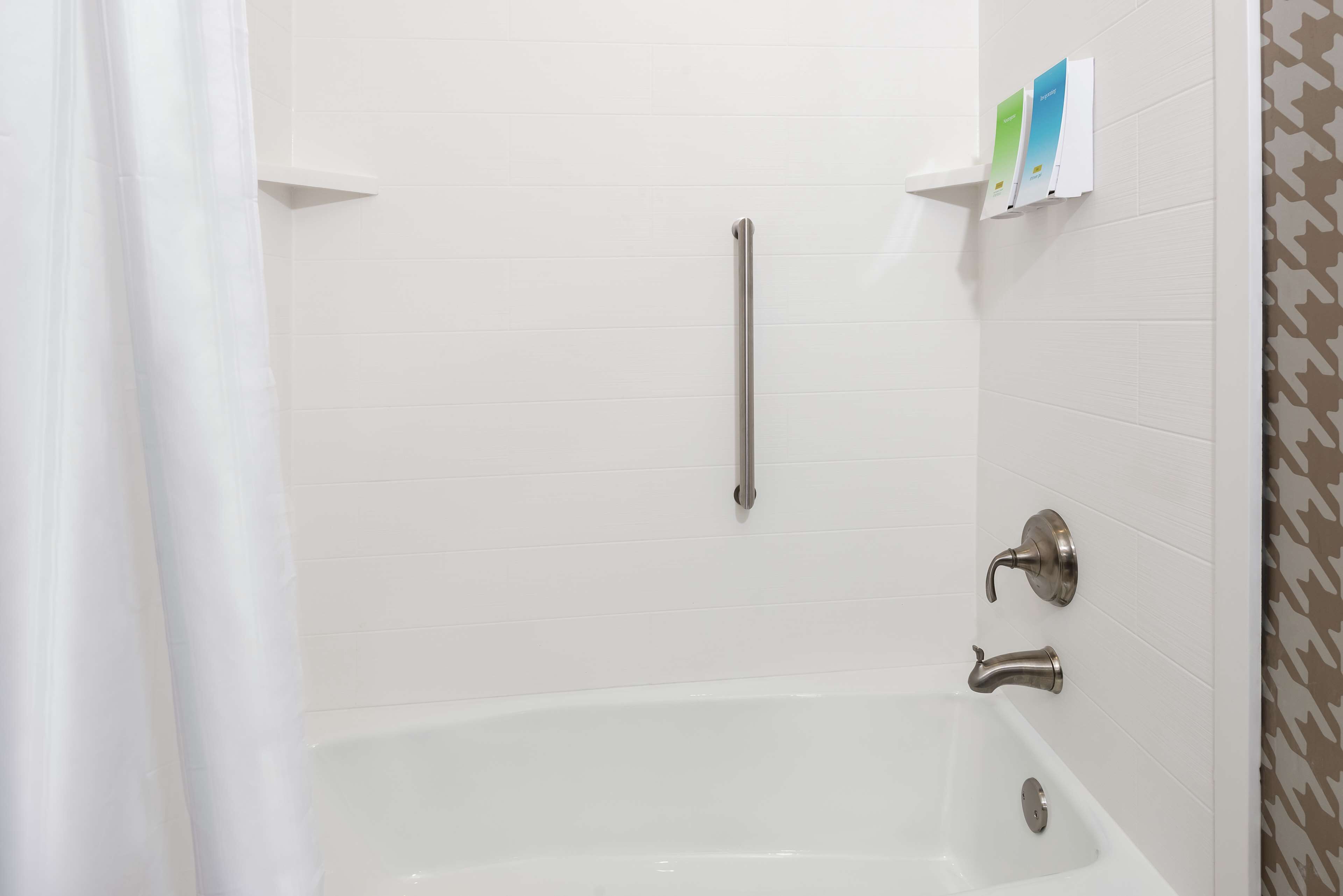 A bathroom with a white bathtub, a handrail, and a towel rack with brochures.