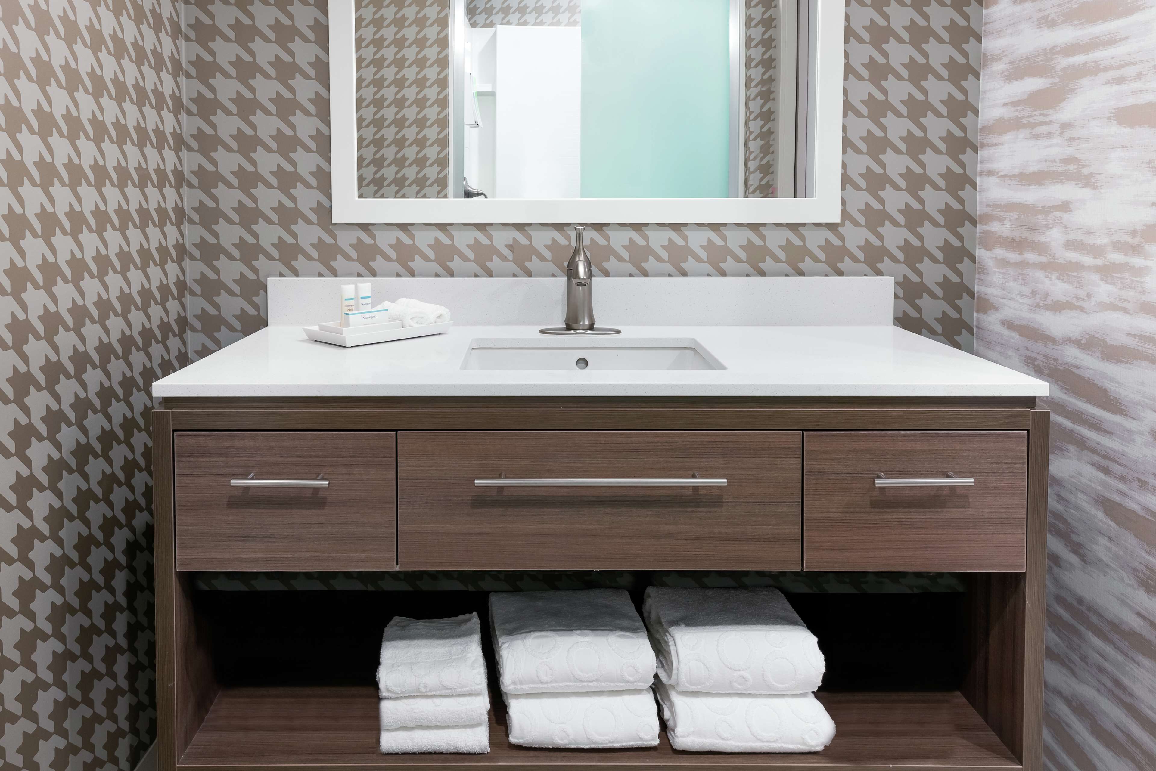 A bathroom with a white sink, a mirror above it, and a towel rack below.