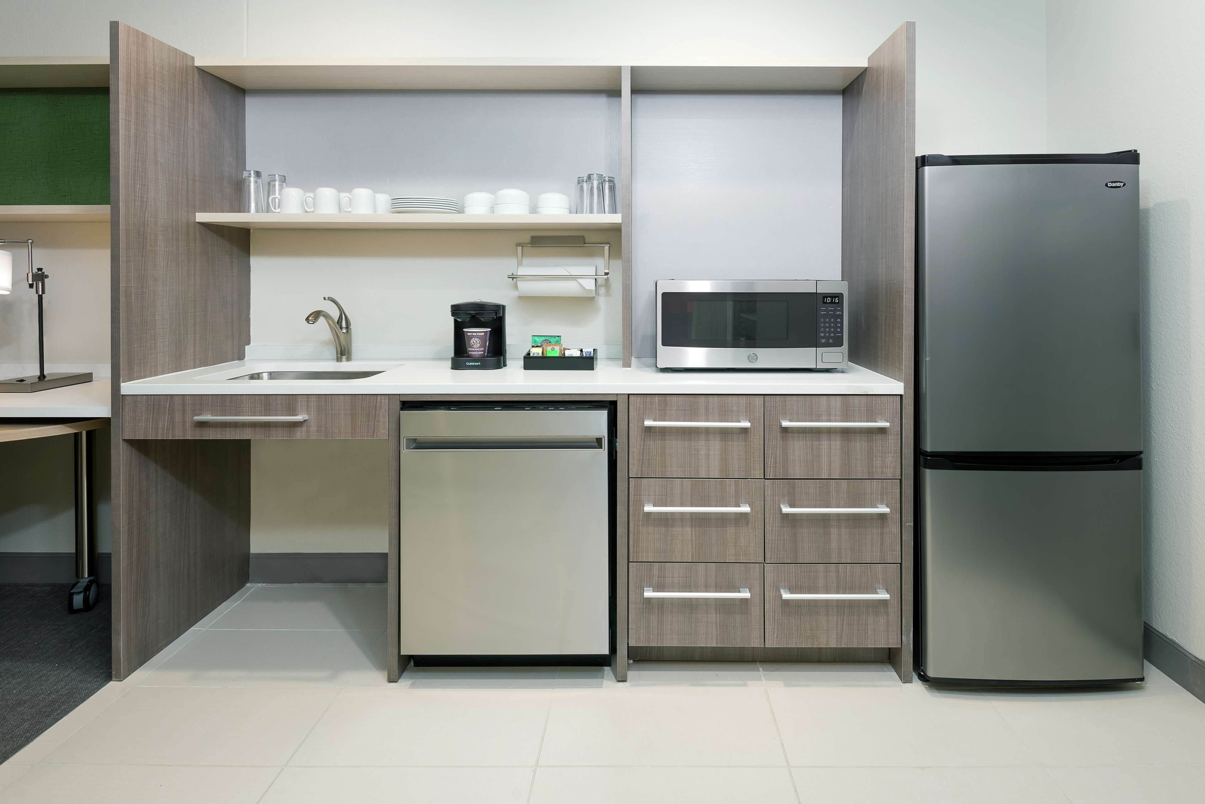 A modern kitchen with a built-in dishwasher, a stainless steel refrigerator, a microwave, and wooden cabinets.