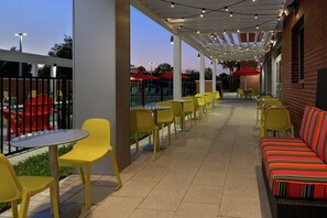 An outdoor patio area with yellow chairs and tables, a striped sofa, and string lights. - Home2 Suites by Hilton Orlando Near UCF (Orlando)
