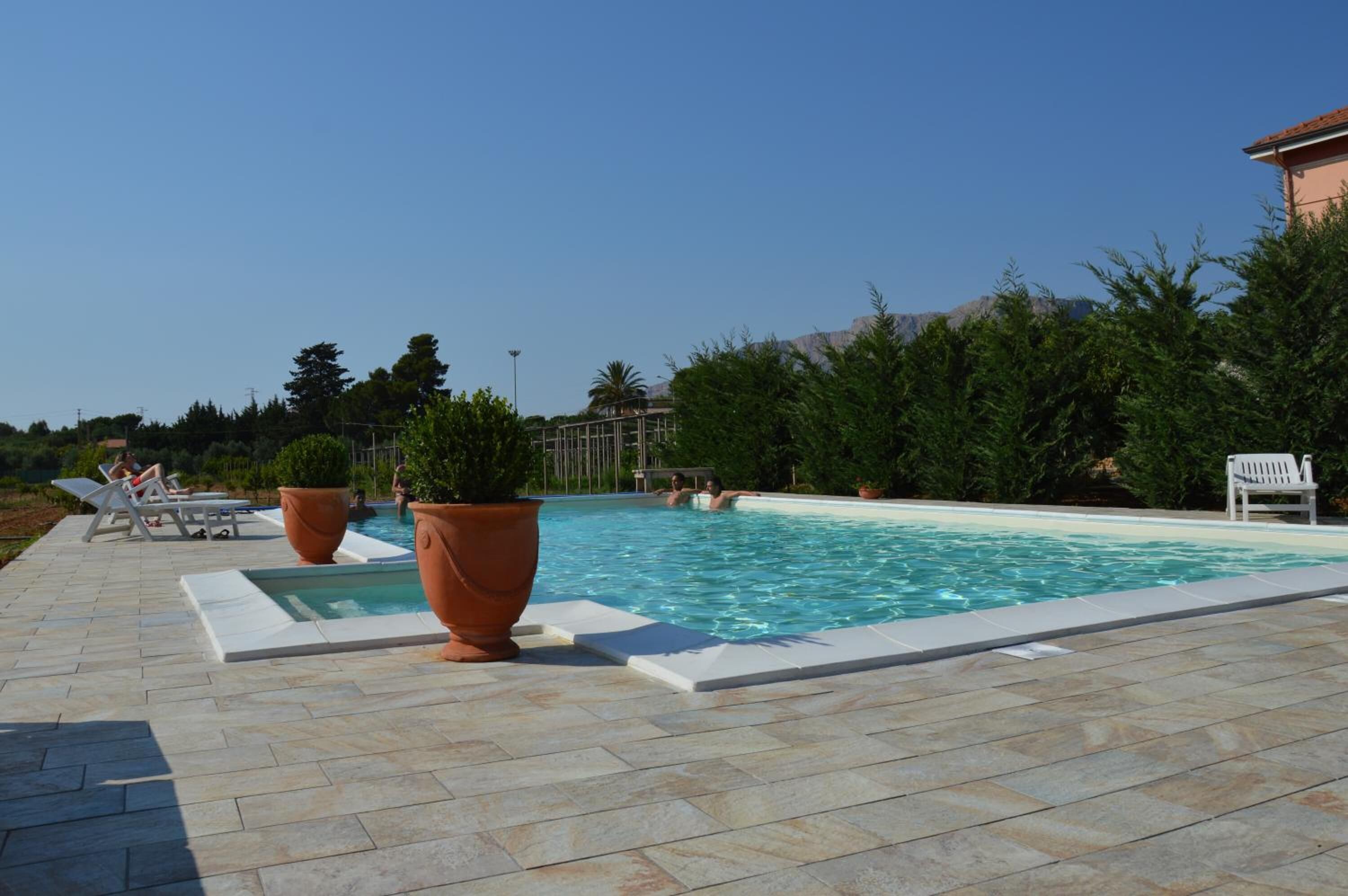 A swimming pool with a tiled deck, surrounded by potted plants and outdoor furniture.