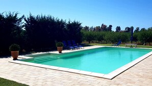 A rectangular swimming pool with a tiled deck, surrounded by potted plants and lounge chairs. - Bed and Breakfast Piano Del Re (Partinico)