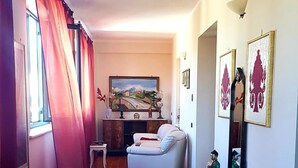 A spacious living room with a sofa, a small table, and a bench. There is a fireplace with a painting above it and a window with curtains. - Bed and Breakfast Piano Del Re (Partinico)
