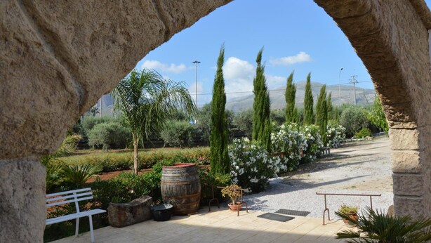 An outdoor garden with a stone archway, a bench, potted plants, and a gravel path. - Bed and Breakfast Piano Del Re (Partinico)