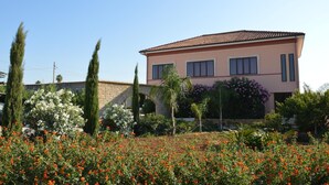 A two-story house with a stone archway, surrounded by a garden with red flowers and various shrubs. - Bed and Breakfast Piano Del Re (Partinico)