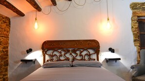A bedroom with a wooden headboard, two bedside lamps, a bed with a white sheet, and a stone wall. - Mas de Tenesa (Benassal)