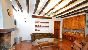 A rustic living room with exposed wooden beams, a leather sofa, a glass coffee table, and shelves with pottery. - Mas de Tenesa (Benassal)