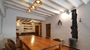 A dining area with a wooden table and chairs, a ceiling with exposed beams, and a wall with a large hole. - Mas de Tenesa (Benassal)