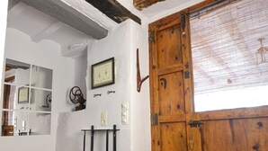 A room with a wooden door, white walls, a tiled floor, and a mirror with shelves. - Mas de Tenesa (Benassal)