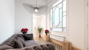 A modern living room with a tufted sofa, a unique pendant light, potted plants, and a patterned floor. - La Casa de Antonio Boutique Rooms (Barcelona)