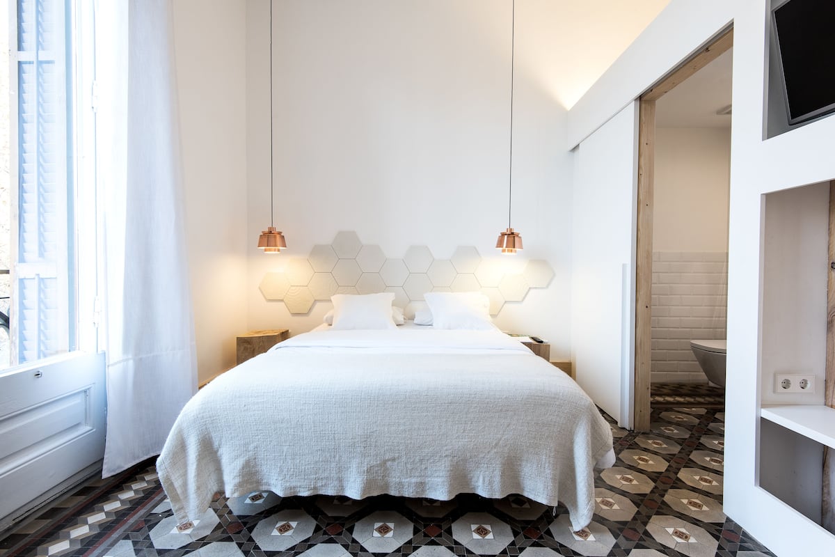 A modern bedroom with a white bed, geometric-patterned floor, and pendant lighting.