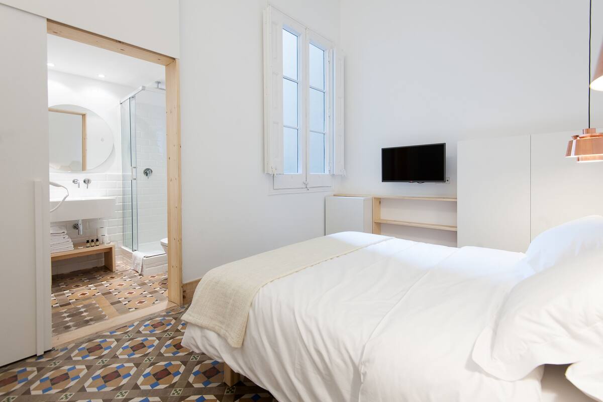 A bedroom with a bed, a TV, a window, and a shower area.