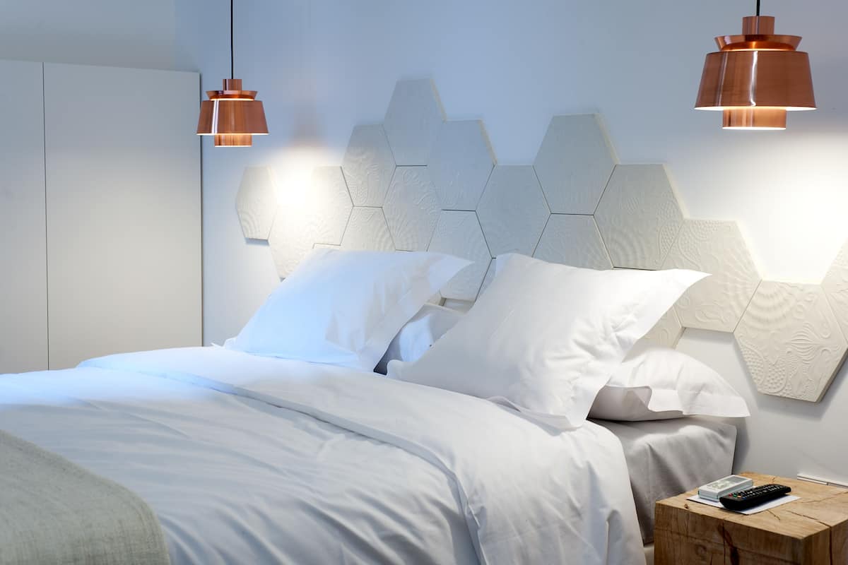 A modern bedroom with a geometric headboard, a neatly made bed with white linens, and a bedside table with a remote control.