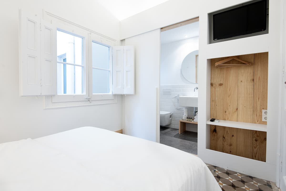 A bedroom with a bed, a wooden wardrobe, and a bathroom visible through an open door.