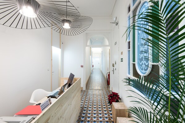 A hotel reception area with a check-in counter, a wooden desk, a patterned floor, and a large window with a decorative frame. - La Casa de Antonio Boutique Rooms (Barcelona)