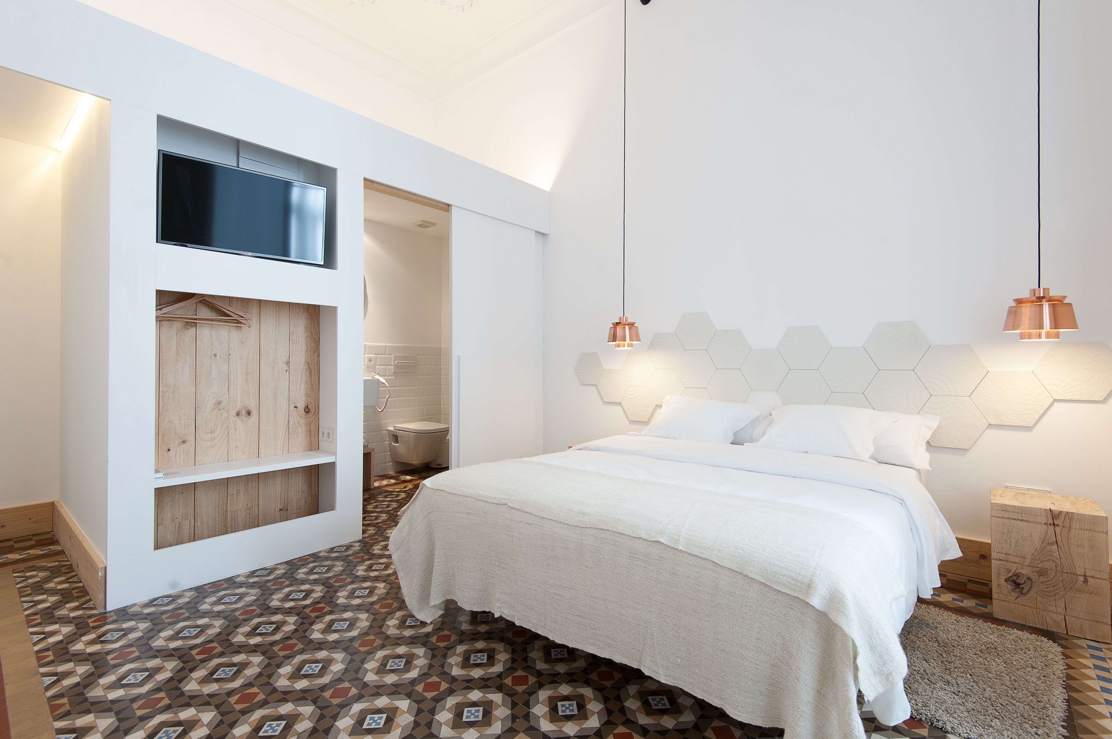 Een moderne slaapkamer met een bed, ingebouwde houten planken, een televisie en vloerbedekking met een geometrisch patroon.