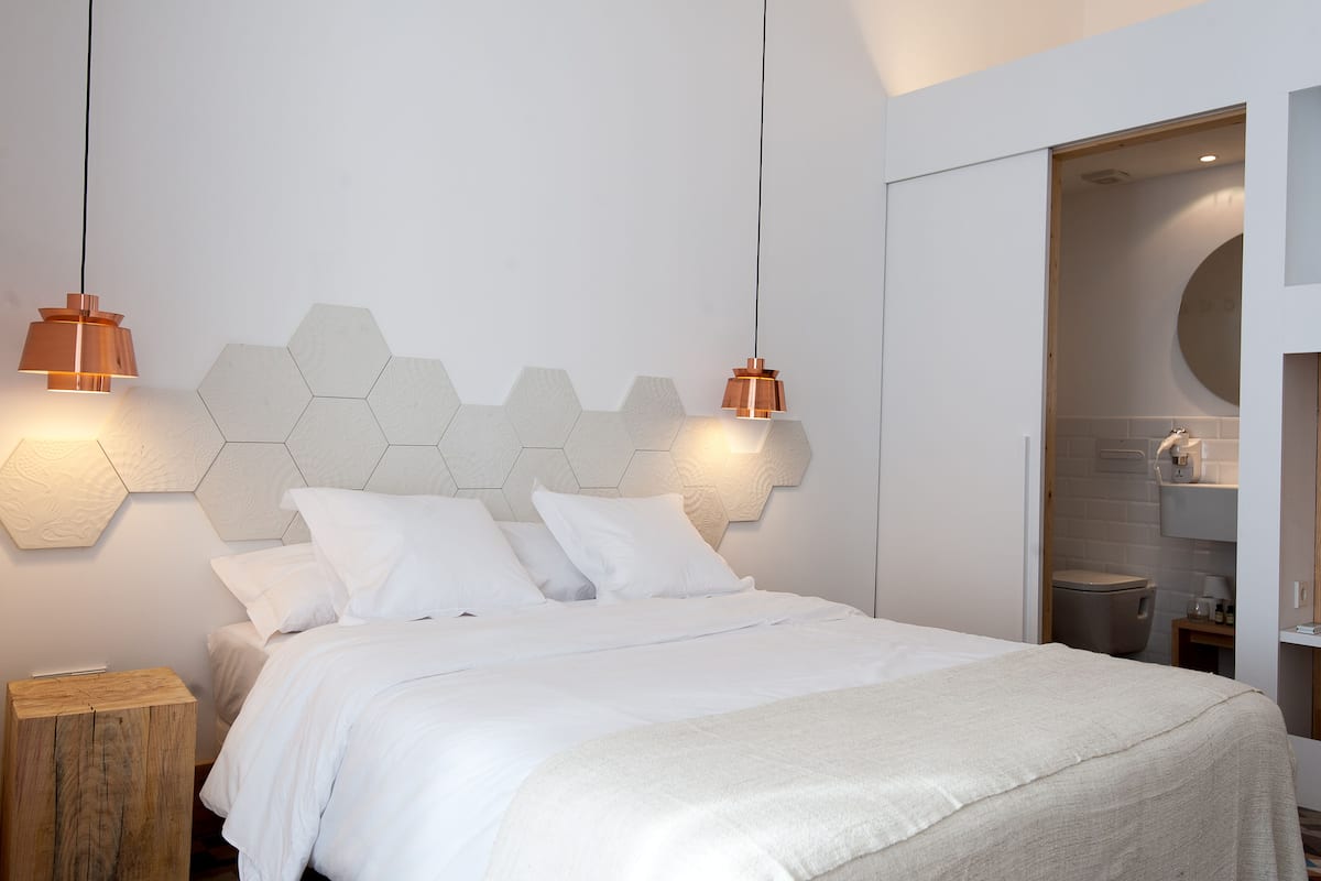 A modern bedroom with a white bed, hexagonal wall headboard, and two pendant lights.