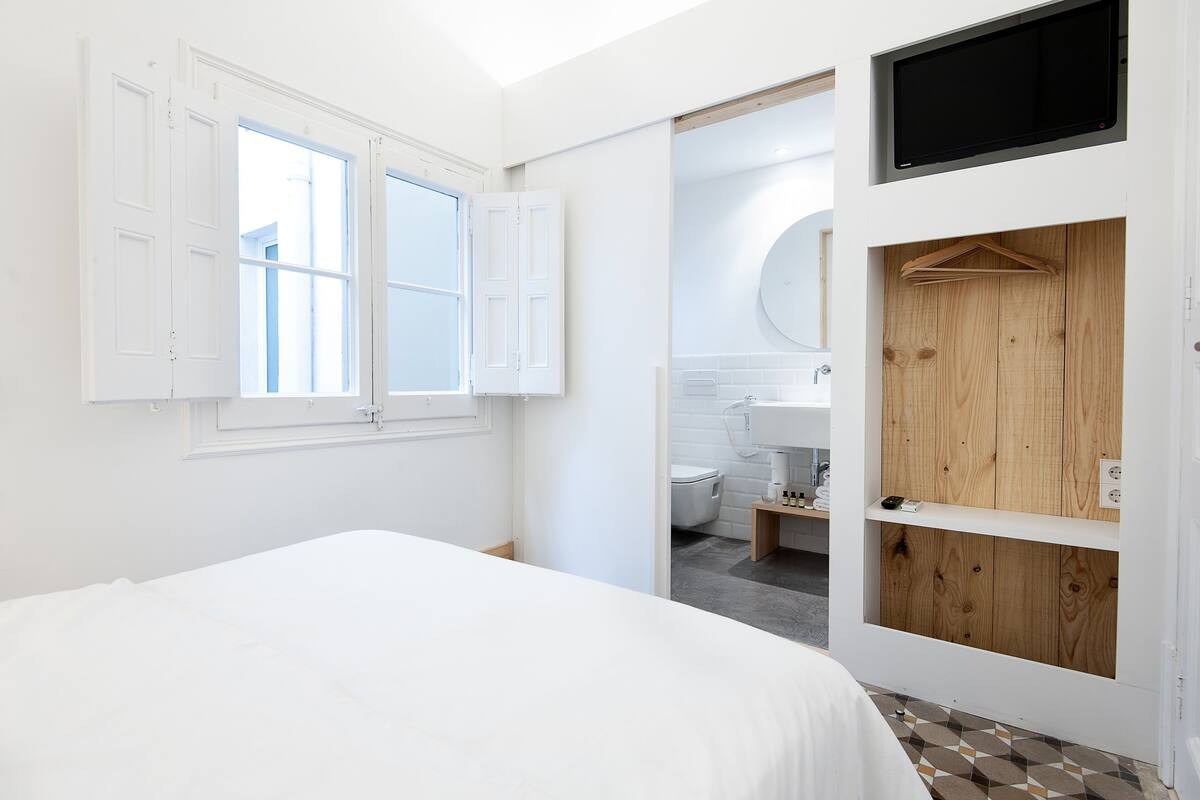 A bedroom with a bed, a white wardrobe, a wooden door, and a bathroom visible through an open door.
