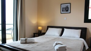 A neatly made bed with a beige quilt and pillows, a bedside lamp, and a framed picture on the wall. - Elina's House (Xylokastro-Evrostina)