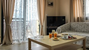 A living room with a sofa, a coffee table with breakfast items, a TV, and sheer curtains. - Elina's House (Xylokastro-Evrostina)