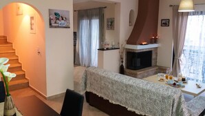 A cozy living room with a fireplace, a dining area with a table set for breakfast, and a staircase leading to another level. - Elina's House (Xylokastro-Evrostina)