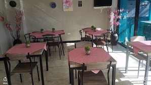 A dining area with round tables covered with pink tablecloths, chairs, and small potted plants.
