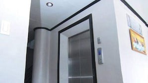 A narrow hallway with a tiled floor, a white wall with a black trim, and an elevator door.