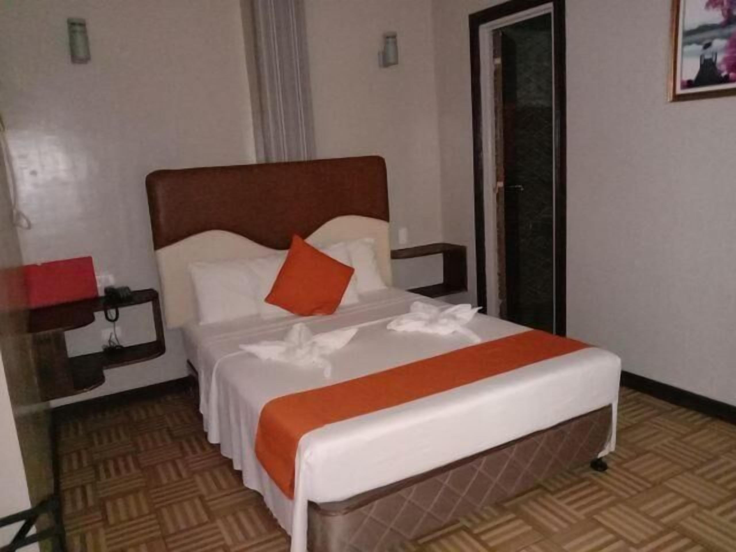 A hotel room with a bed, a nightstand, a red object on the nightstand, and a door.