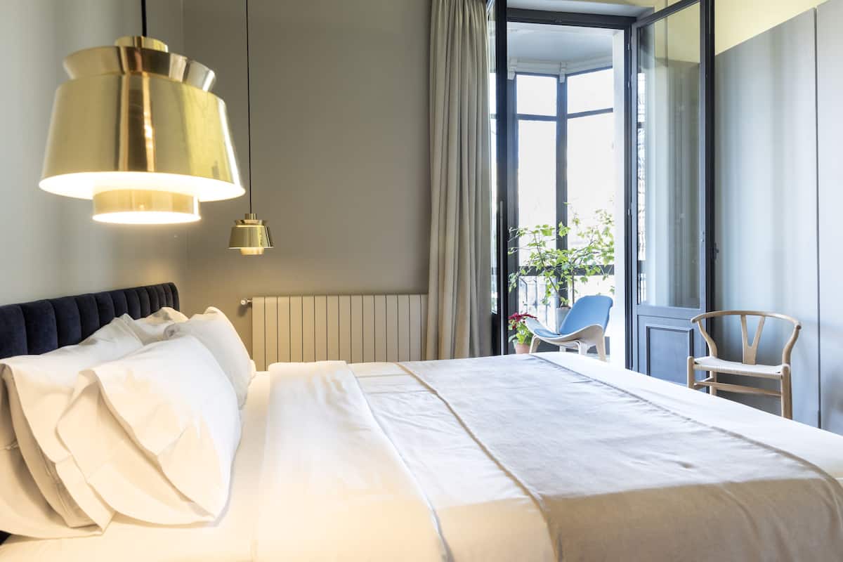 Hotelkamer met een groot bed, een hanglamp, uitzicht op het omliggende landschap en een stoel bij het raam.