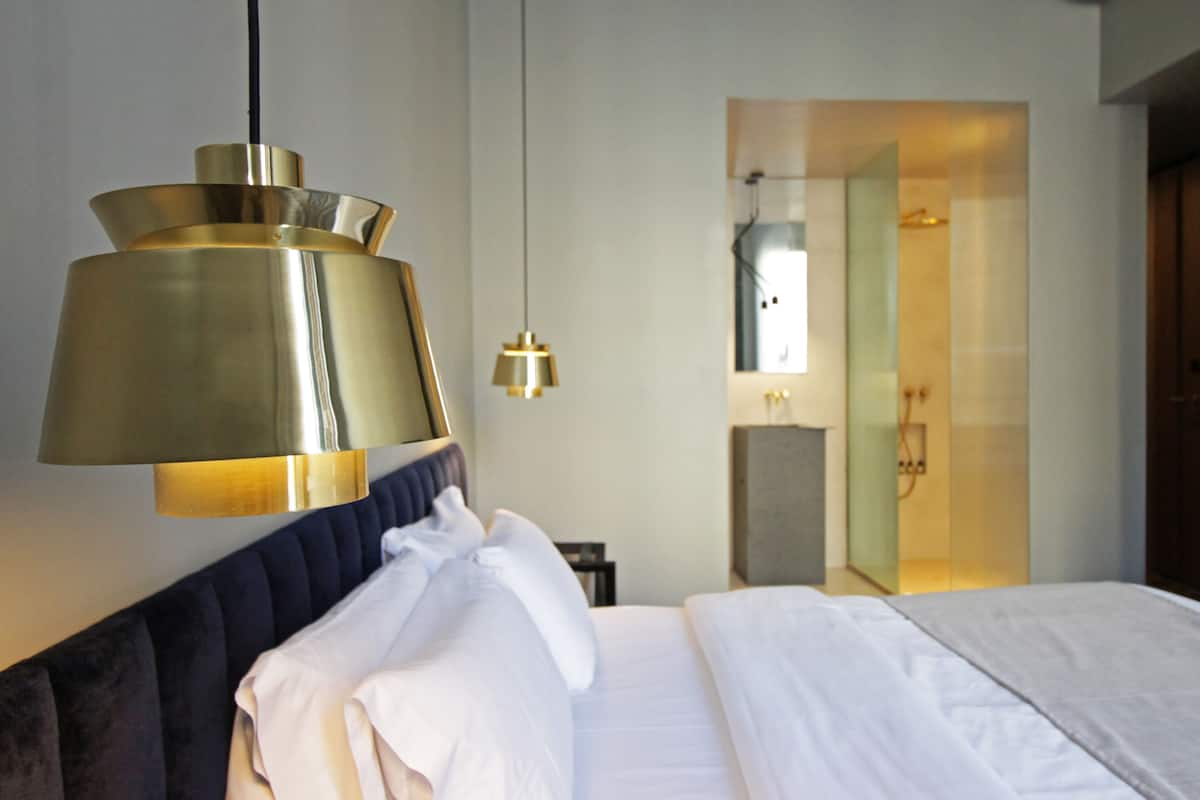 Een hotelkamer met een bed, een hanglamp, een spiegel en een douchehoek.