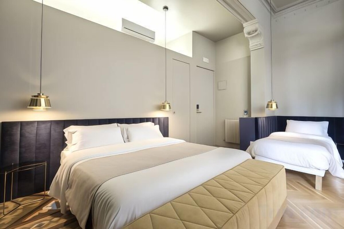 Habitación de hotel con dos camas, un espejo grande e iluminación colgante.