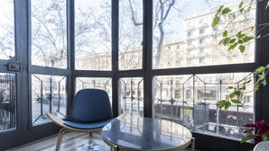 Une pièce avec une grande fenêtre, une chaise bleue, une petite table et un sol à motifs.