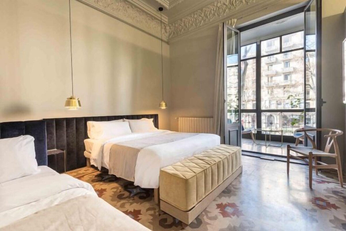 Habitación de hotel con dos camas, un ventanal grande y vistas a edificios.