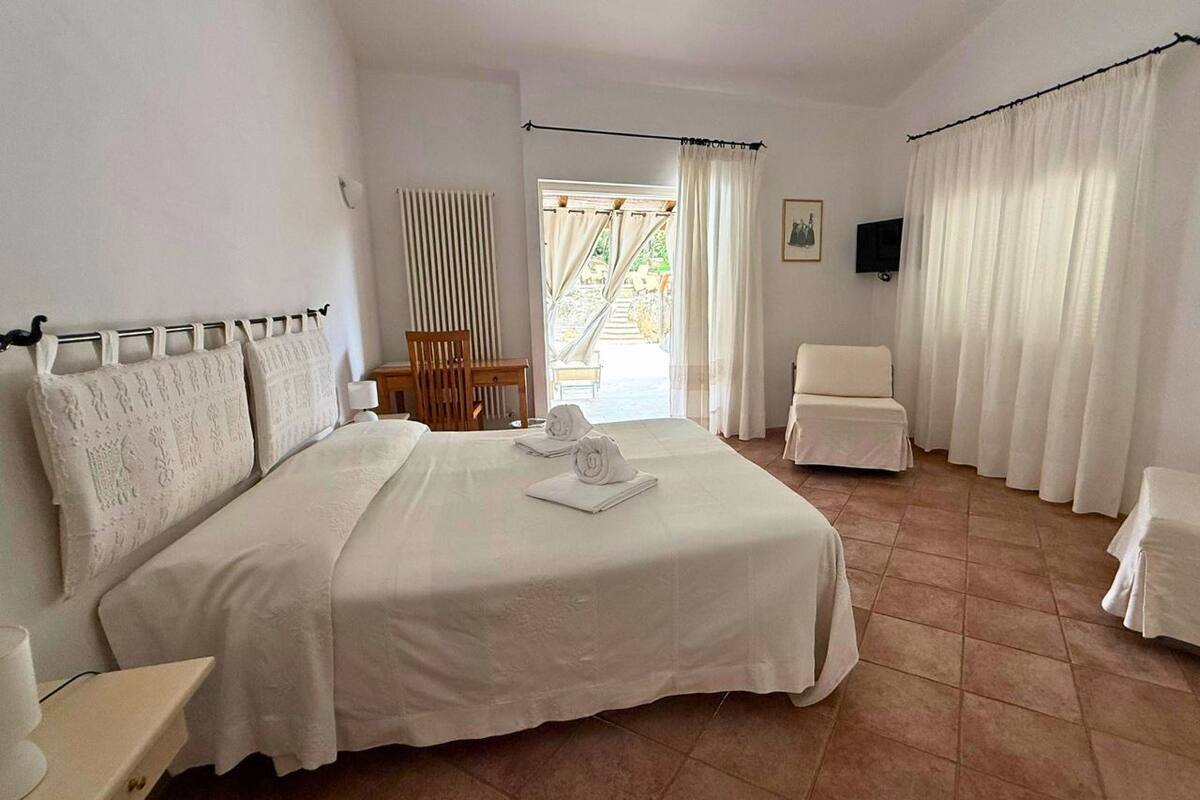 A hotel room with a large bed, a chair, a small table, and a view of the outside.
