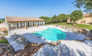 A swimming pool with a tiled deck, a covered seating area, and a stone wall surrounding the pool.
