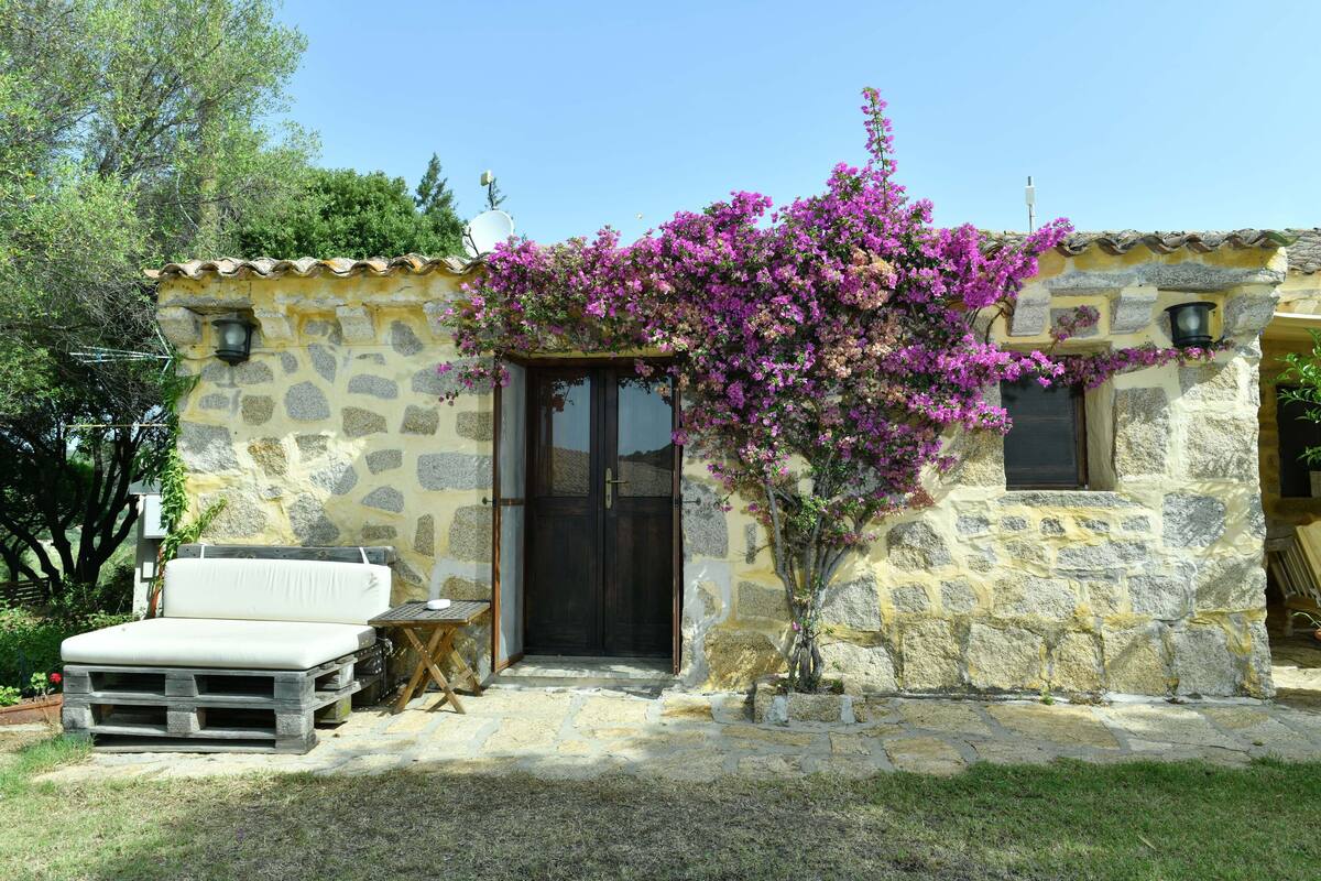 A stone house with a wooden door, a small porch, and a white sofa.
