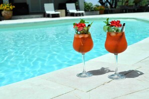 Two cocktails with garnishes by a poolside.