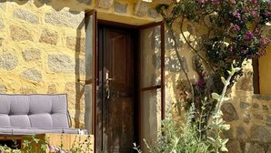 A stone building with a wooden door and a cushioned bench outside. - Lu Pastruccialeddu (Arzachena)