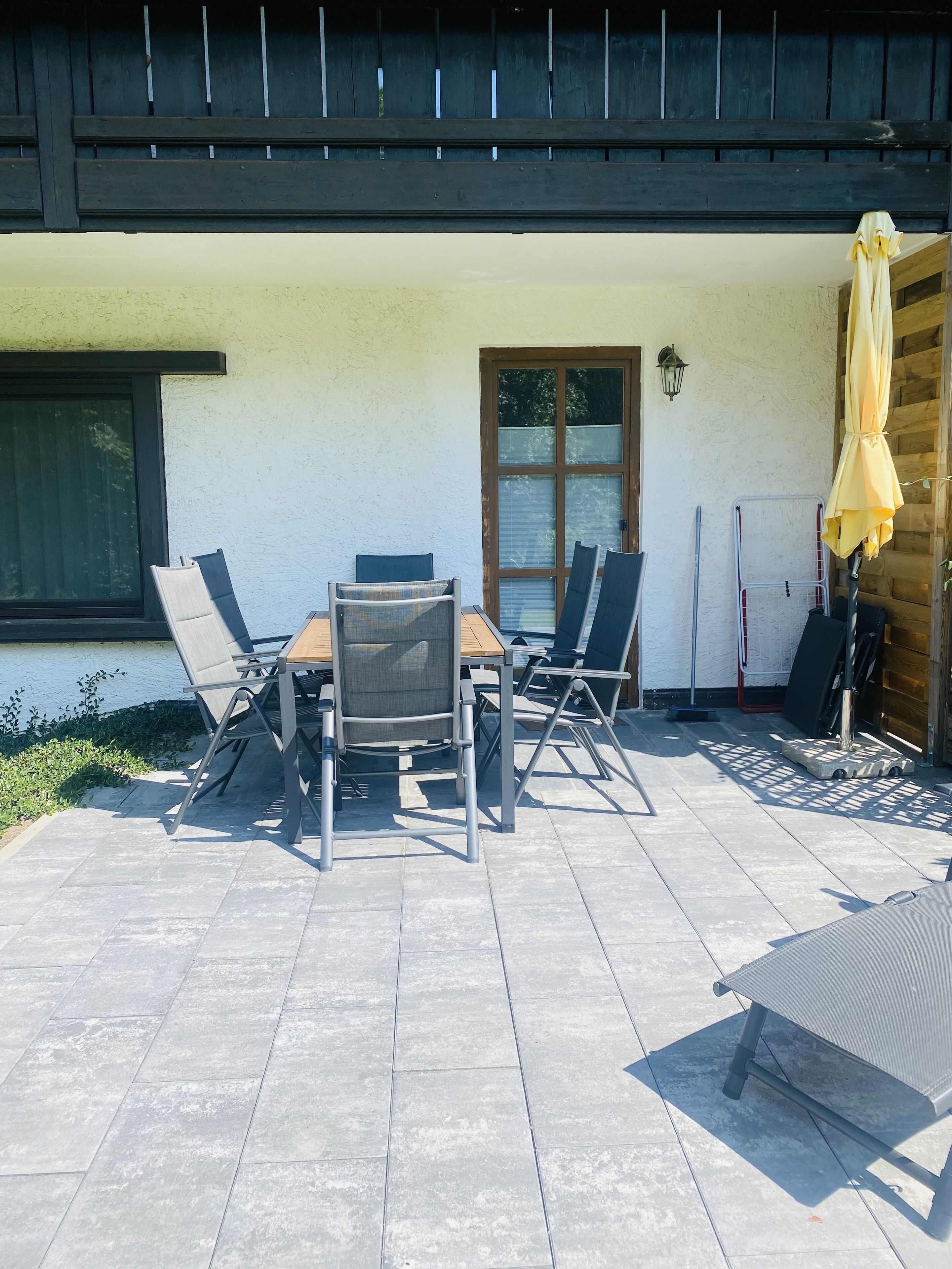 Une terrasse extérieure avec une table et des chaises, une porte-fenêtre coulissante et un parasol jaune.