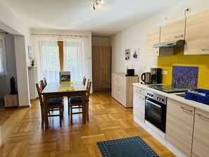 A modern kitchen with wooden cabinets, a dining table with chairs, and a built-in oven. - Ferienwohnungen Bachblick (Uebersee)