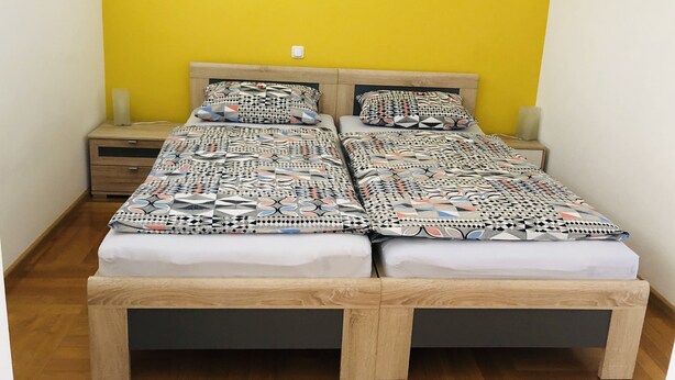 Una cama doble con ropa de cama estampada, una mesita de noche con lámpara y un banco de madera.