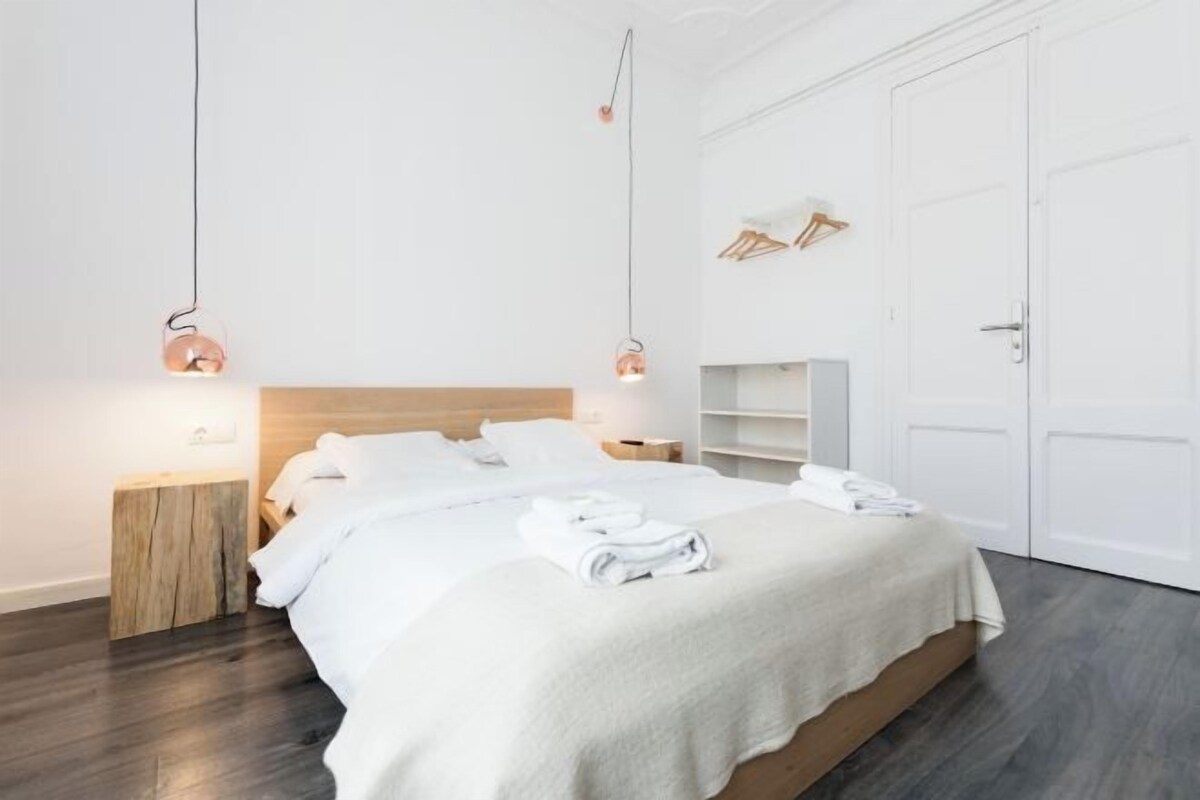 Una habitación de hotel moderna con una cama grande, cabecera de madera, ropa de cama blanca y un armario empotrado.