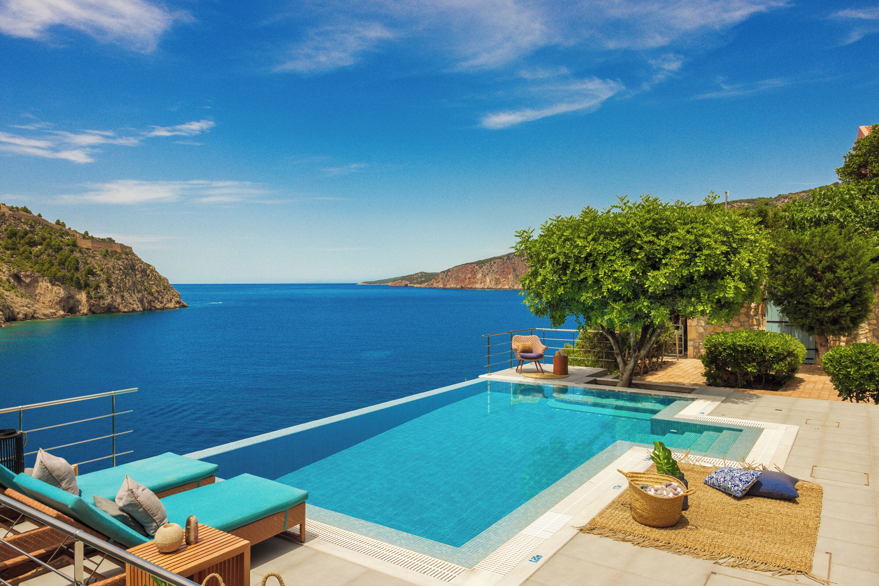 Una piscina con vista al mar, sillas de descanso y una pequeña mesa con una cesta.